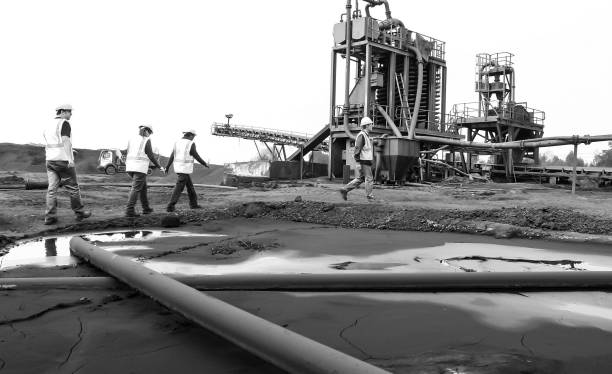 an oil worker is pouring water from a gas well while workers look at a pipeline Johannesburg, South Africa – April 02, 2024: Oil worker empties water from gas well as colleagues inspect pipeline Oil Industry in Africa stock pictures, royalty-free photos & images